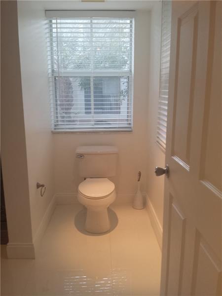 A small bathroom with white walls, tile flooring, a toilet, and a window with blinds — 2451 E Centergate Drive # 208, Miramar FL 33025, MIRAMAR, FL