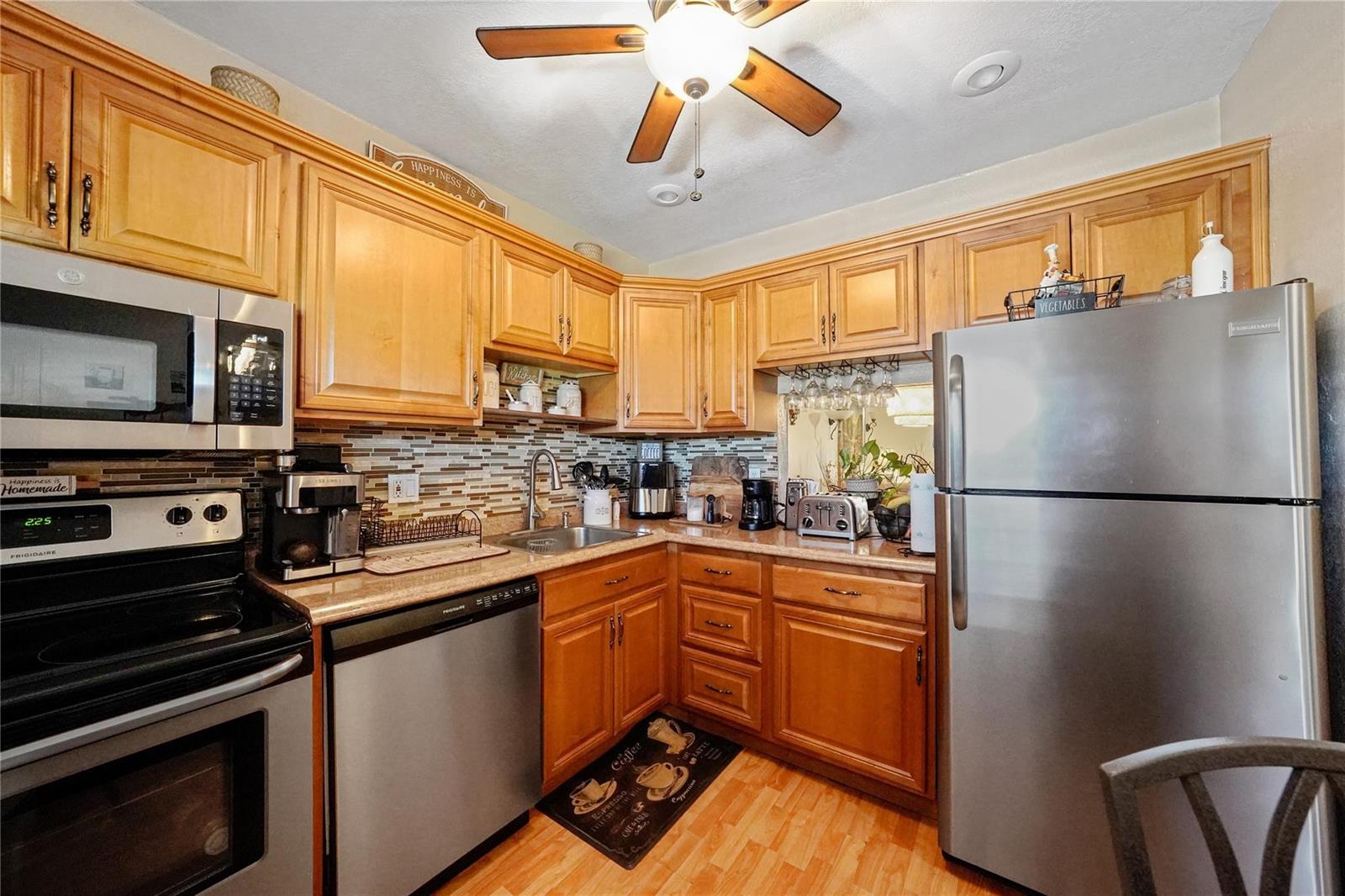 A kitchen features light wood cabinets, stainless steel appliances, and a mosaic tile backsplash — 551 NW 76th Terrace # 208, Margate FL 33063, MARGATE, FL