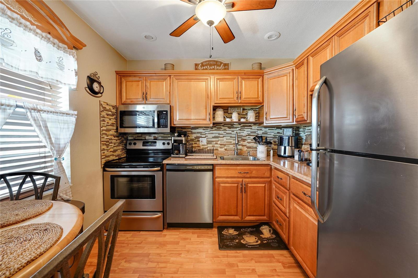 A kitchen features wood cabinets, stainless steel appliances, a tiled backsplash, and a dining area — 551 NW 76th Terrace # 208, Margate FL 33063, MARGATE, FL