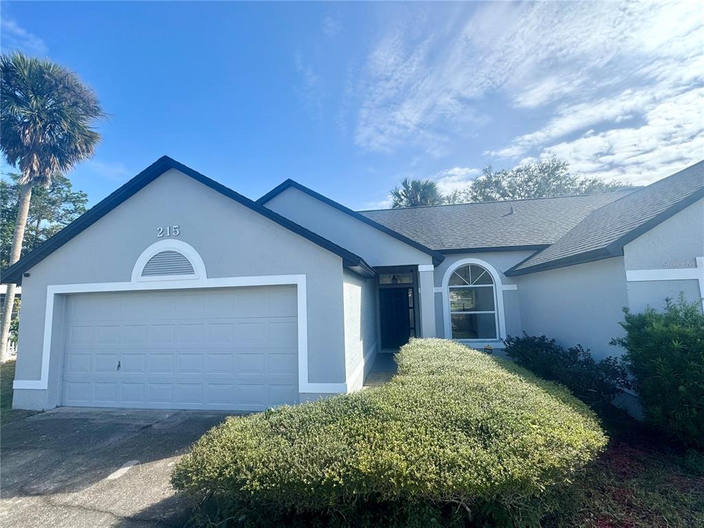 A single-story house with a gray exterior, a two-car garage, and a manicured front hedge — 215 HOLLOWBROOK CIRCLE, DAYTONA BEACH, FL
