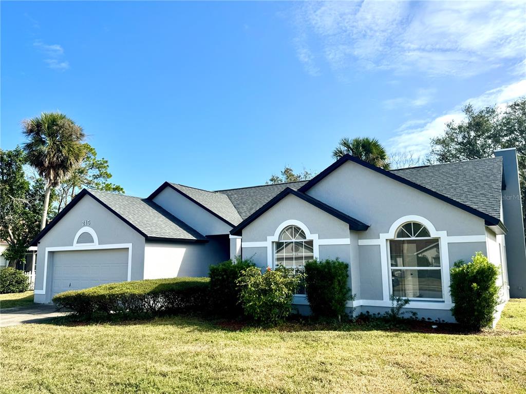 A single-story house with a gray exterior, dark roof, and arched windows under a blue sky — 215 HOLLOWBROOK CIRCLE, DAYTONA BEACH, FL