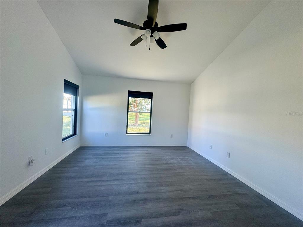 An empty room features white walls, gray wood-look flooring, a ceiling fan, and two windows — 215 HOLLOWBROOK CIRCLE, DAYTONA BEACH, FL