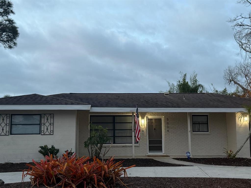 A single-story house with a light-colored brick exterior, a front porch, and an American flag — 5004 MEDALIST ROAD, SARASOTA, FL