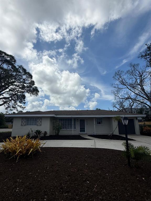 A single-story house with a light-colored exterior, a brown roof, and a paved driveway — 5004 MEDALIST ROAD, SARASOTA, FL