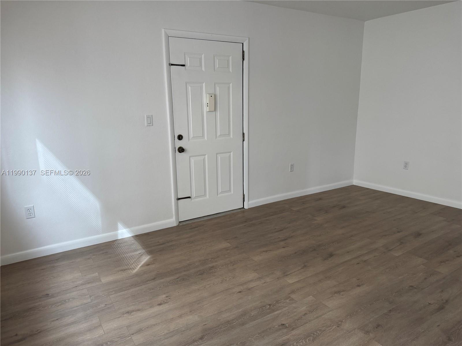 An empty room features white walls, wood-look laminate flooring, and a white entry door — 4080 SW 2nd Ter # 6, Miami FL 33134, MIAMI, FL