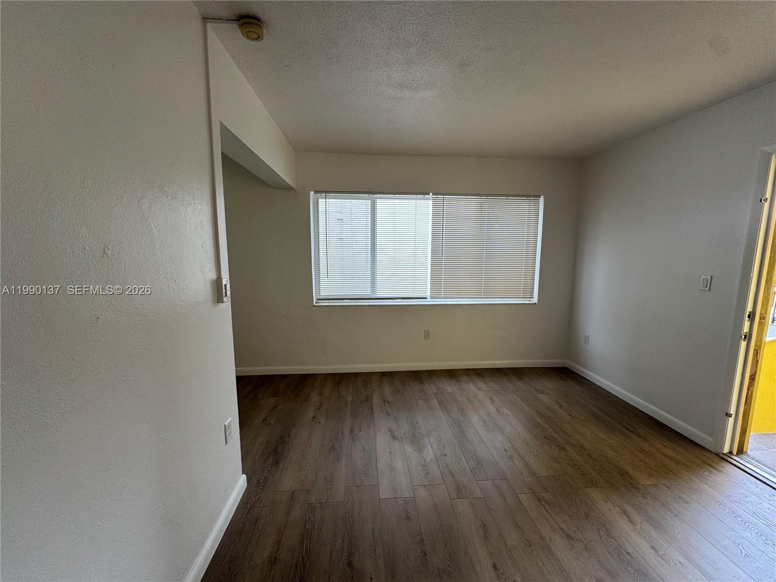 An empty room features wood-look flooring, white walls, and a window with horizontal blinds — 4080 SW 2nd Ter # 6, Miami FL 33134, MIAMI, FL