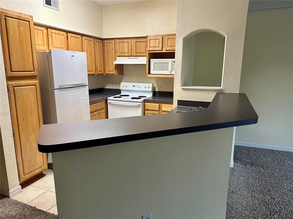 A kitchen features wood cabinets, white appliances, dark countertops, and a breakfast bar — 3446 SOHO STREET UNIT 206, ORLANDO, FL