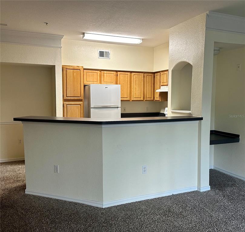 A kitchen with light wood cabinets, a white refrigerator, and a black breakfast bar counter — 3446 SOHO STREET UNIT 206, ORLANDO, FL
