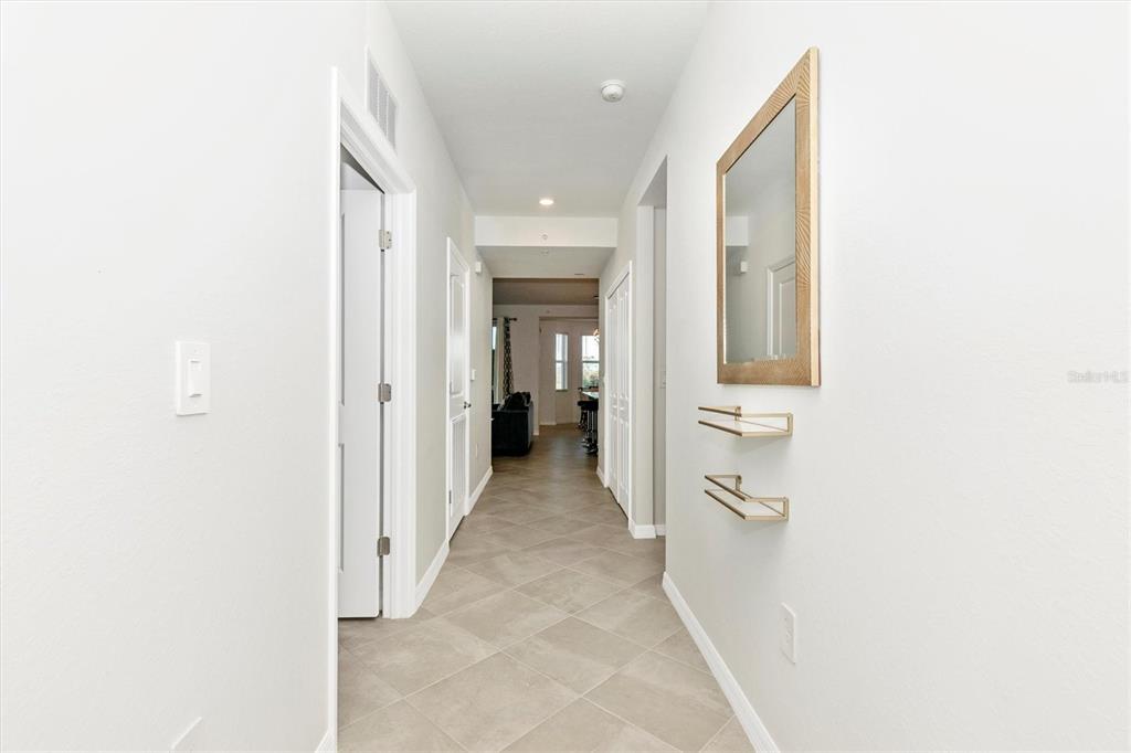 A hallway with light-colored tile flooring, white walls, a mirror, and two small wall shelves — 17565 OPAL SAND DRIVE UNIT 102, VENICE, FL