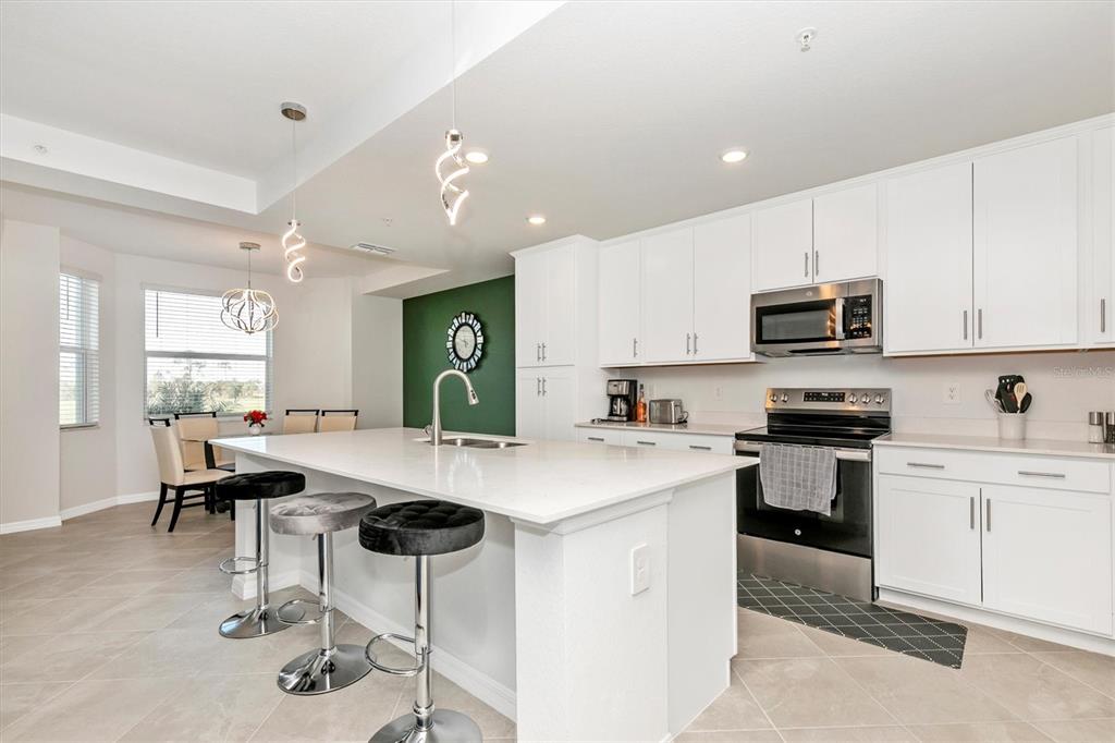 A modern kitchen features white cabinetry, a large quartz island with bar stools, and stainless appliances — 17565 OPAL SAND DRIVE UNIT 102, VENICE, FL