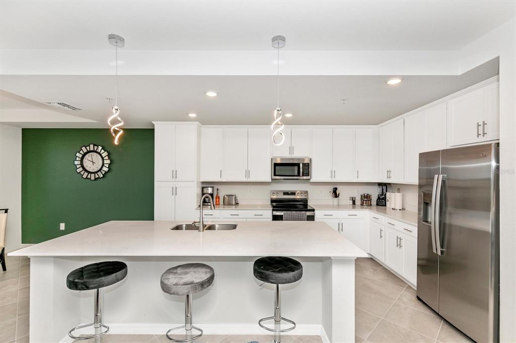 A modern kitchen features white cabinetry, a large island with bar stools, and green wall — 17565 OPAL SAND DRIVE UNIT 102, VENICE, FL