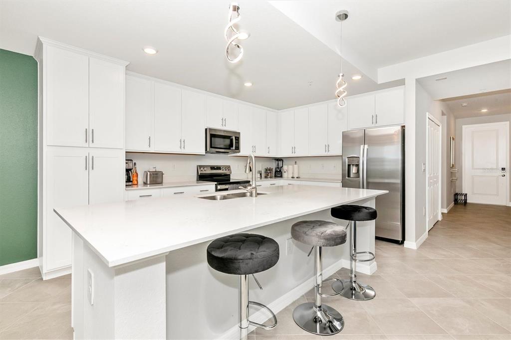 A modern kitchen features white cabinets, a large quartz island, and three black bar stools — 17565 OPAL SAND DRIVE UNIT 102, VENICE, FL
