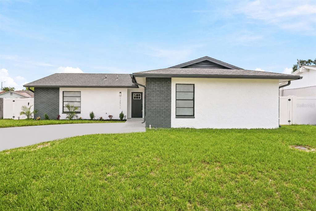 A single-story house with white stucco, dark brick accents, and a gray shingled roof — 12511 CARDIFF DRIVE, TAMPA, FL