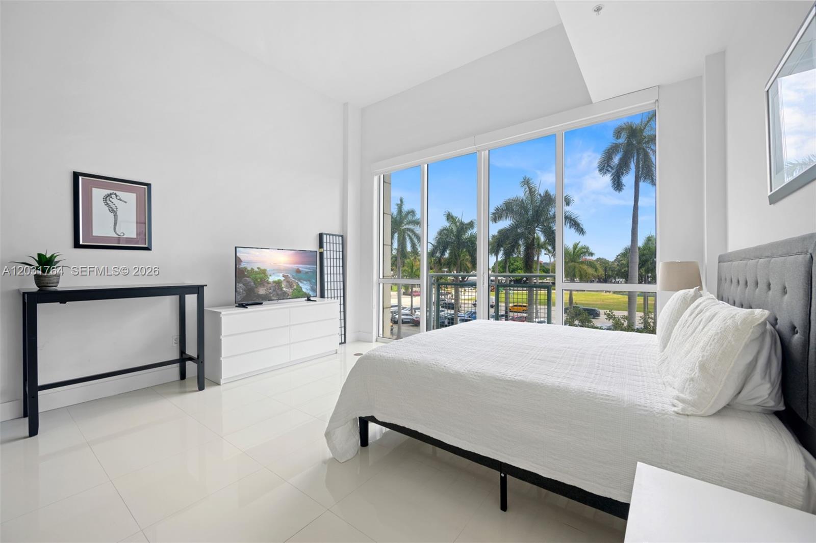 A modern bedroom features white tile floors, a bed, and floor-to-ceiling windows with palm trees — 253 NE 2nd St # 231, Miami FL 33132, MIAMI, FL