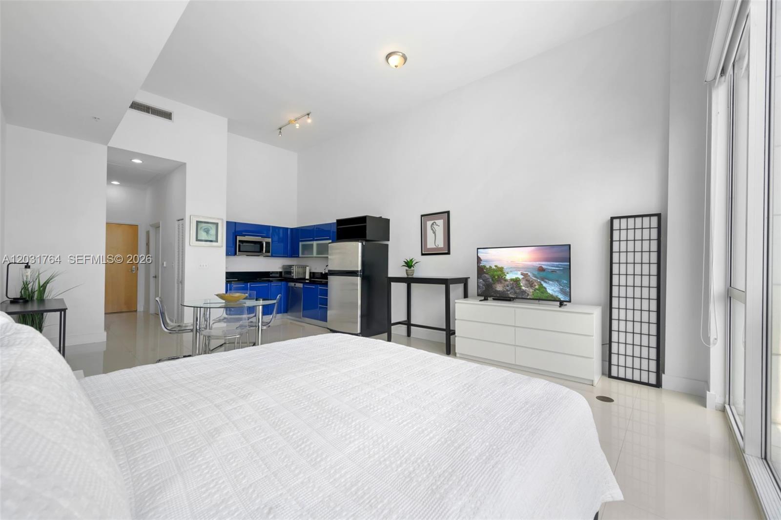 A studio apartment features a white bed, blue kitchen cabinets, and a television on a dresser — 253 NE 2nd St # 231, Miami FL 33132, MIAMI, FL