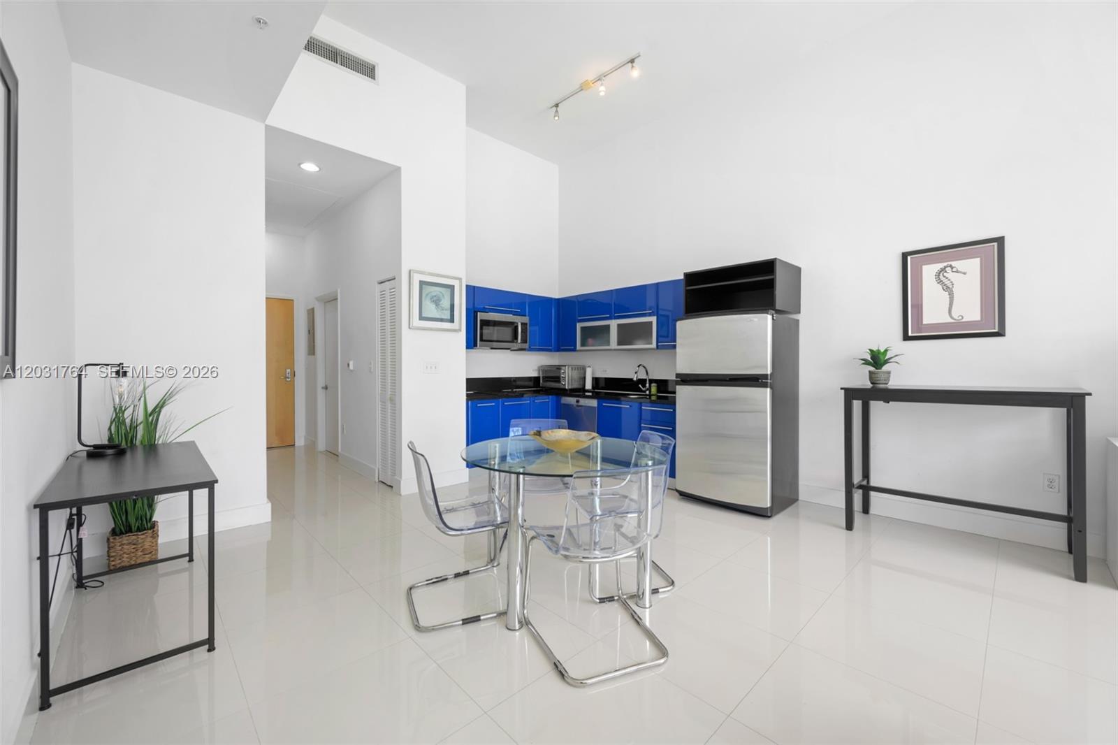 A modern kitchen features blue cabinets, a glass dining table, and white tile flooring — 253 NE 2nd St # 231, Miami FL 33132, MIAMI, FL