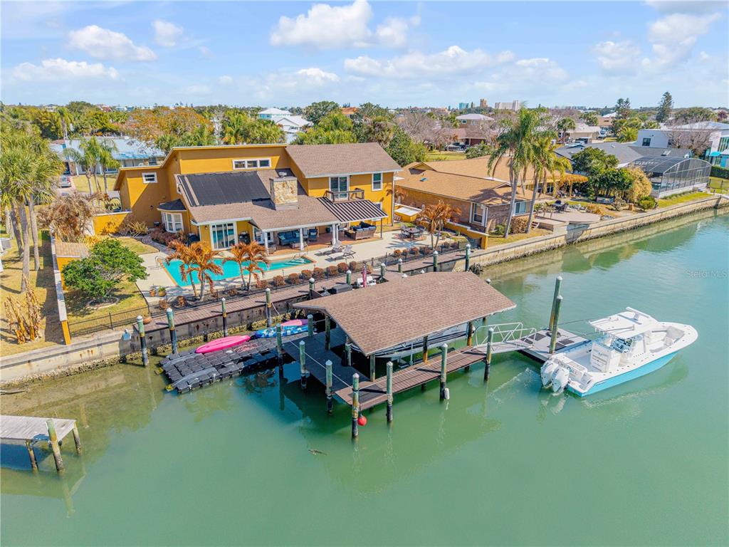 An aerial view of a yellow waterfront house with a pool, dock, and boat lift — 102 VIA DUOMO, NEW SMYRNA BEACH, FL