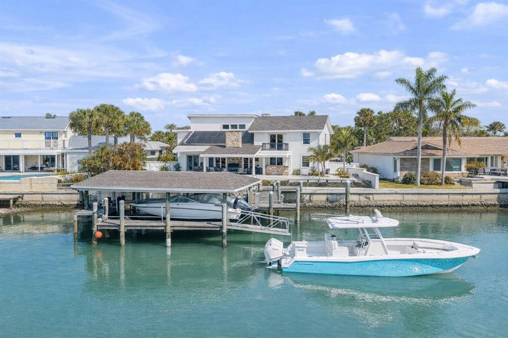 A waterfront house with a boat lift and a docked boat on a canal — 102 VIA DUOMO, NEW SMYRNA BEACH, FL