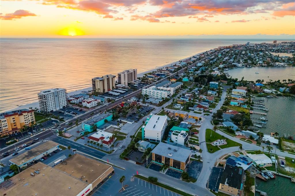 An aerial view shows a coastal town with high-rise buildings, residential homes, and a beach — 15305 1ST STREET E UNIT 201, MADEIRA BEACH, FL