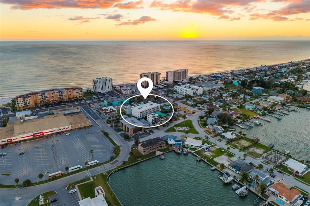 An aerial view shows a multi-story building circled near a beach, parking lot, and waterway — 15305 1ST STREET E UNIT 201, MADEIRA BEACH, FL