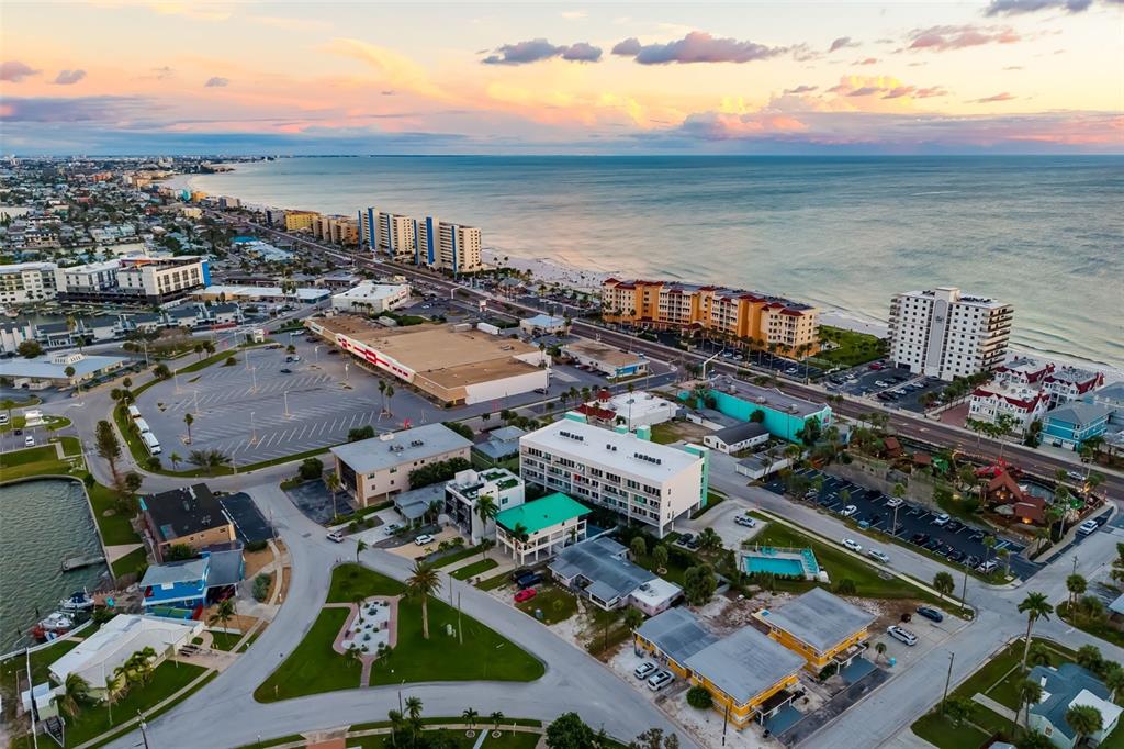 An aerial view shows a coastal town with hotels, a large parking lot, and the ocean — 15305 1ST STREET E UNIT 201, MADEIRA BEACH, FL