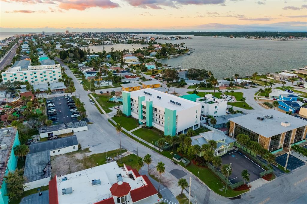 An aerial view shows a multi-story white and teal apartment building near a coastal waterway — 15305 1ST STREET E UNIT 201, MADEIRA BEACH, FL