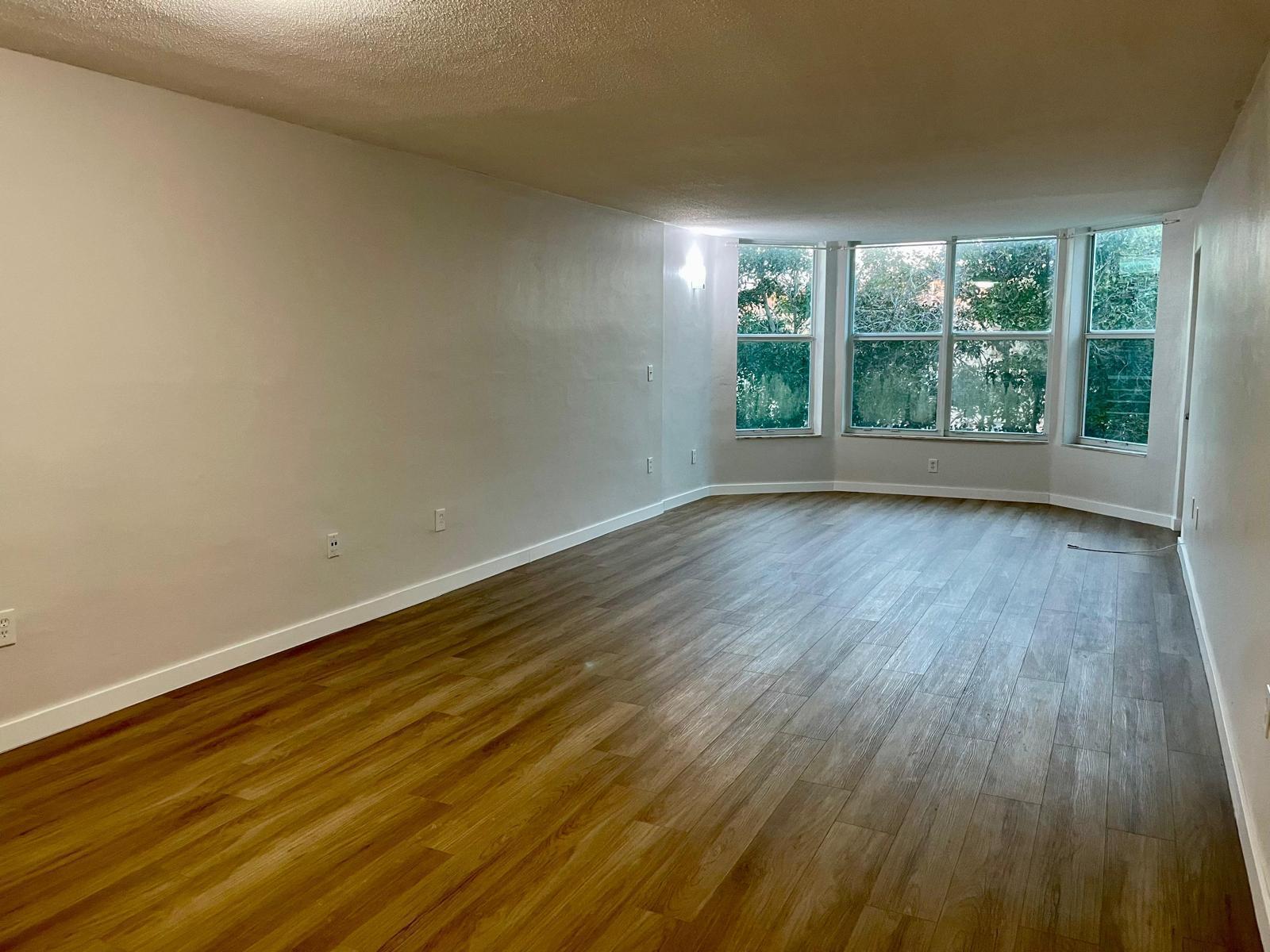 An empty living room with light-colored walls, wood-look flooring, and a large bay window — 1401 NE 191st Street, Miami FL 33179, MIAMI, FL