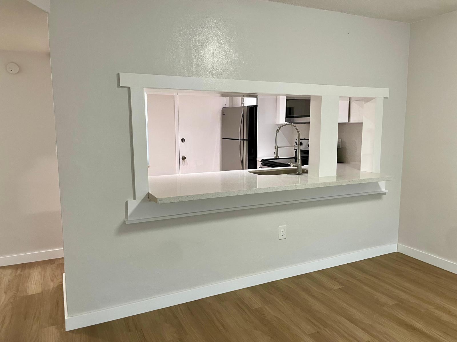 A kitchen pass-through window with a white frame and quartz countertop overlooks a modern kitchen — 1401 NE 191st Street, Miami FL 33179, MIAMI, FL
