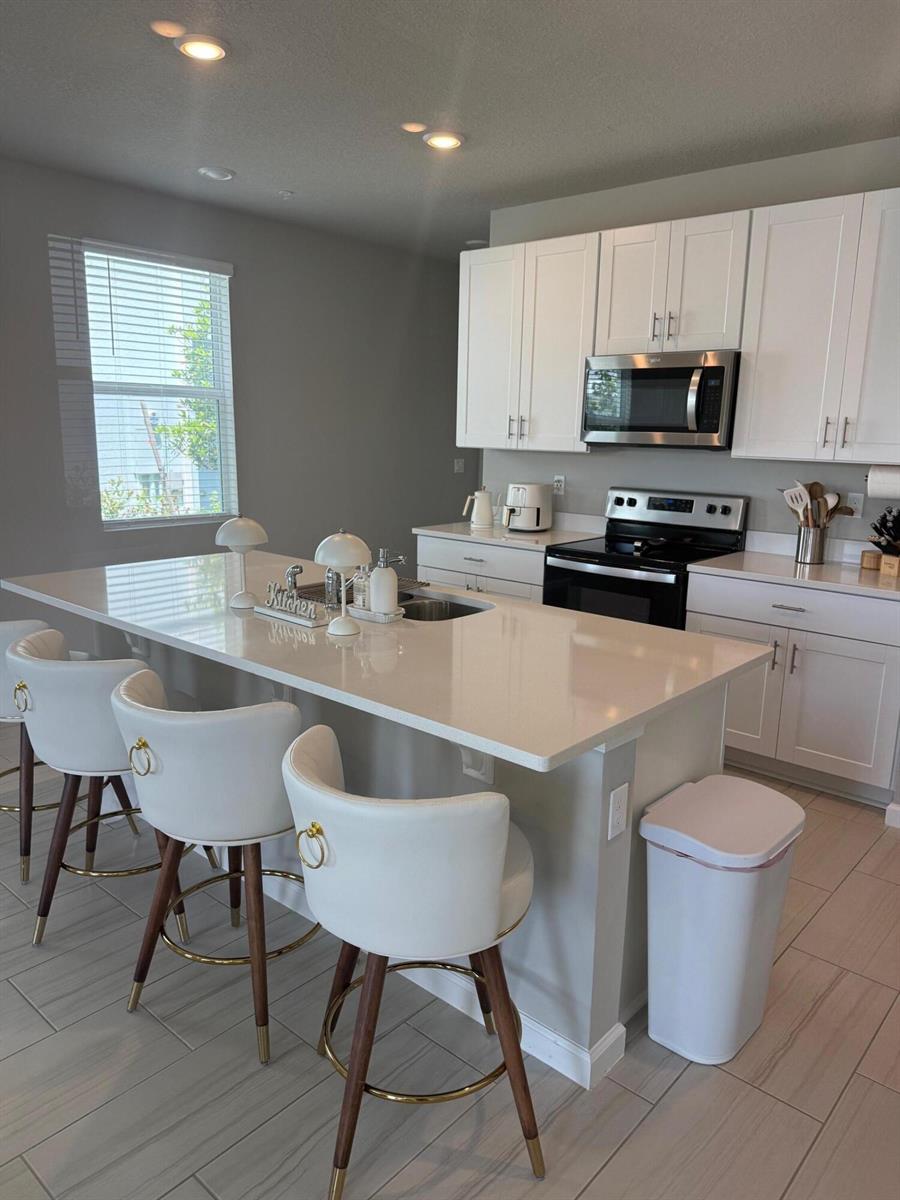 A kitchen features white cabinetry, a large quartz island with bar stools, and tile flooring — 389 Salisbury Circle, Fort Pierce FL 34982, FORT PIERCE, FL