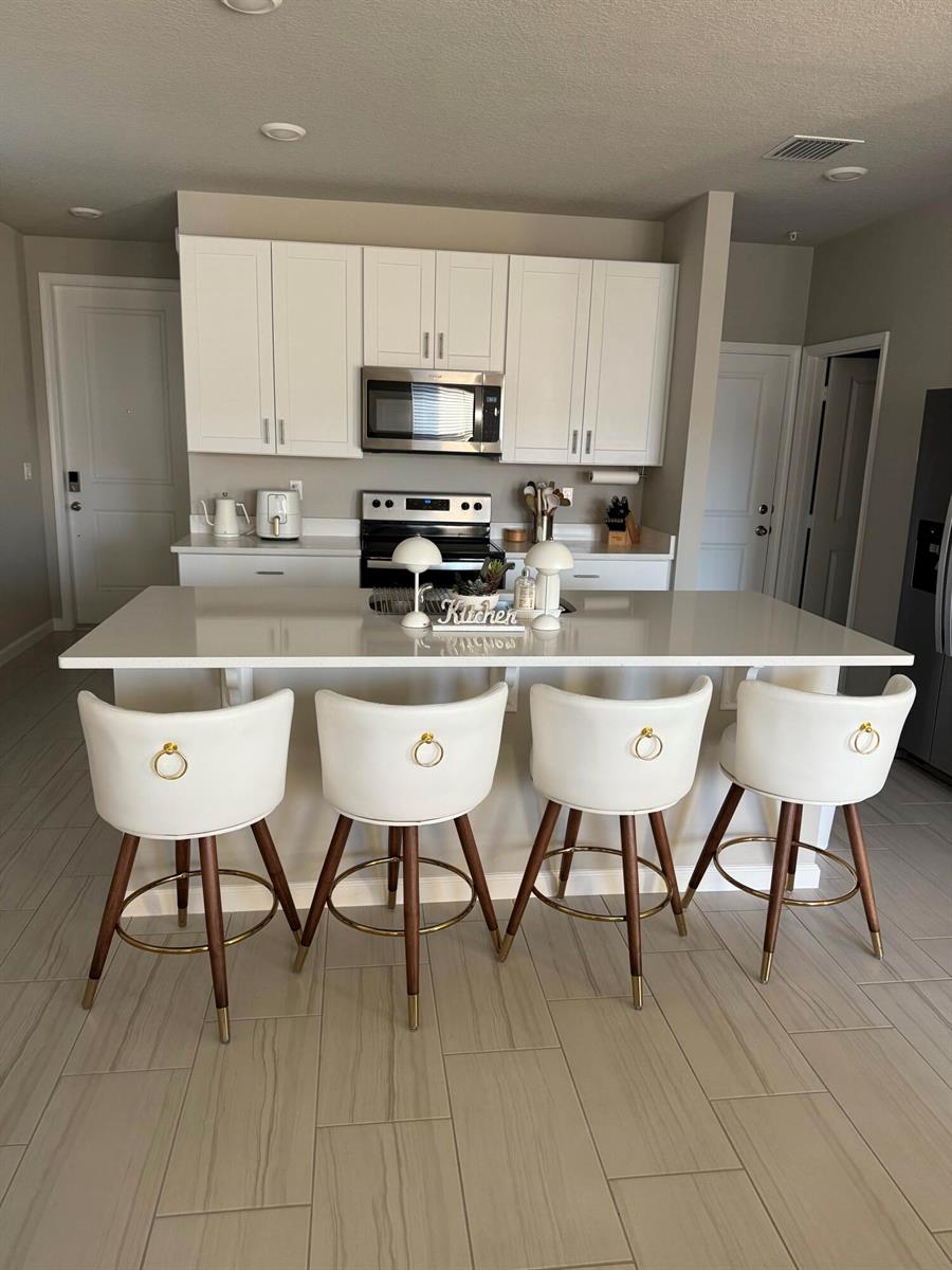 A modern kitchen features white cabinetry, a quartz island, and four white bar stools — 389 Salisbury Circle, Fort Pierce FL 34982, FORT PIERCE, FL