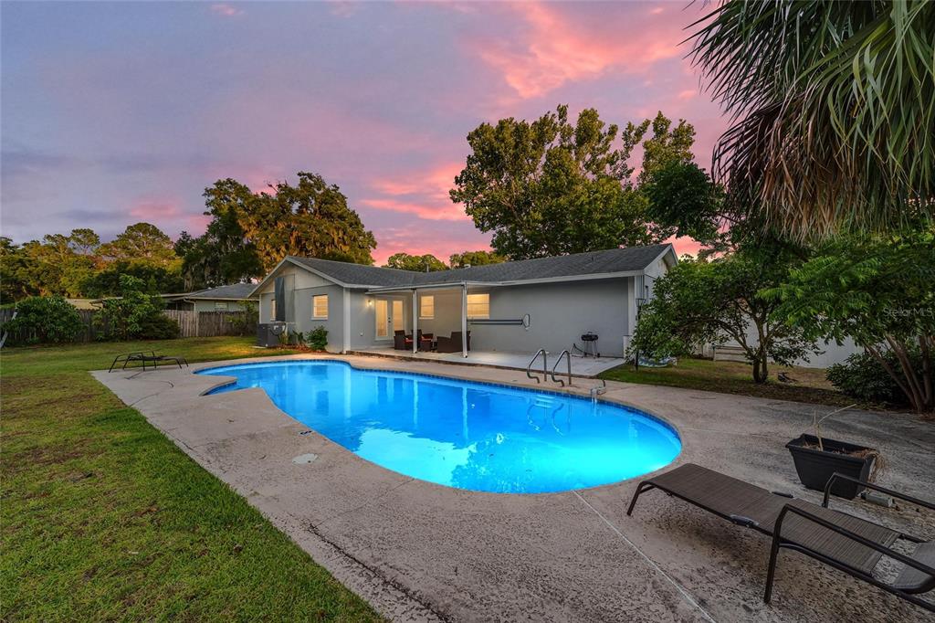 A backyard features a swimming pool, a concrete patio, and a single-story house at sunset — 3823 SE 9TH PLACE, OCALA, FL