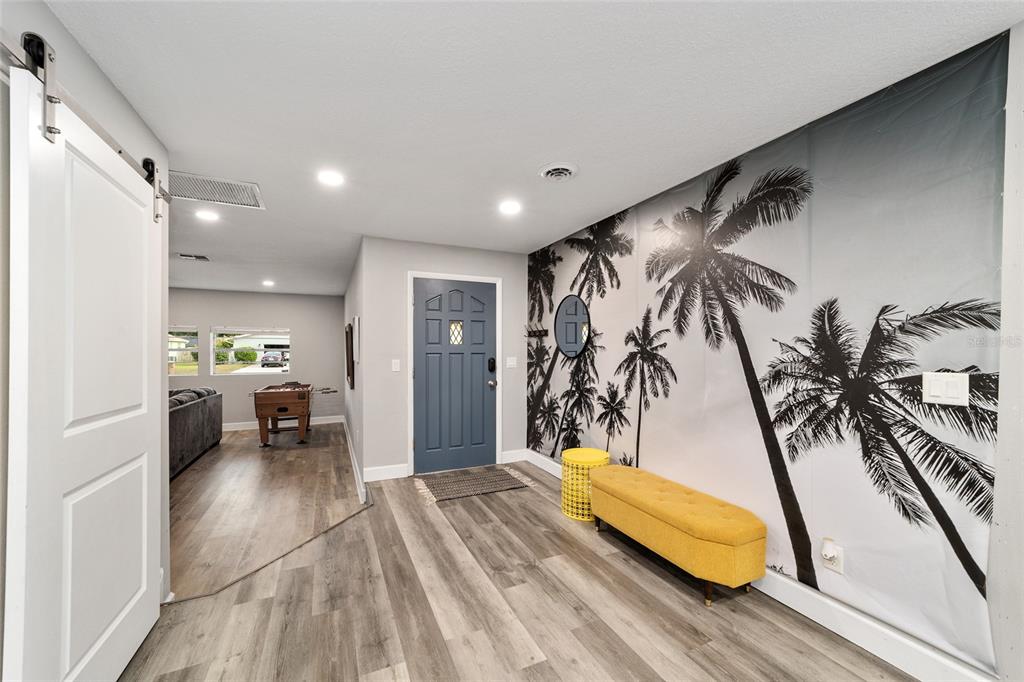 An entryway features gray wood-look flooring, a blue front door, and a palm tree wall mural — 3823 SE 9TH PLACE, OCALA, FL