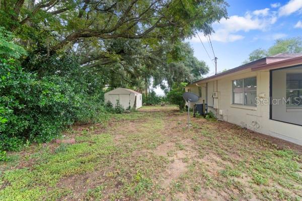 The backyard features a small storage shed, a large tree, and the side of a house — 1404 E ALFRED STREET, TAVARES, FL