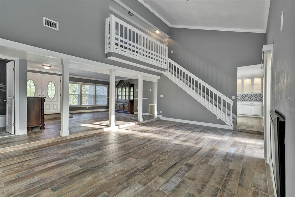 A spacious living area features wood-look tile flooring, a staircase with white railings, and columns — 1879 KAMLER AVENUE, ORLANDO, FL