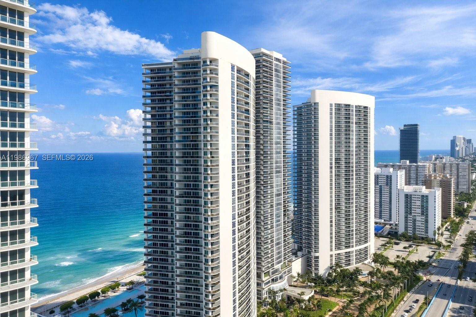An aerial view shows three tall residential towers situated along a sandy beach and ocean — 1800 S Ocean Dr, Hallandale Beach FL 33009, HALLANDALE BEACH, FL