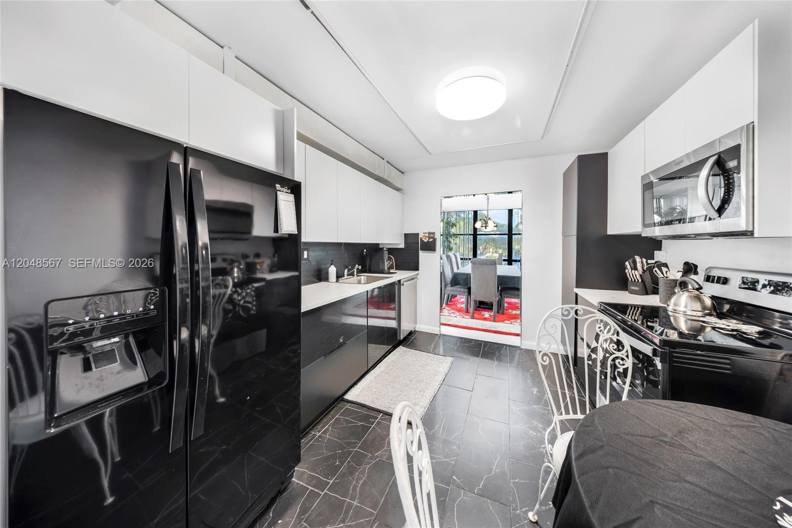 A modern kitchen features black appliances, white upper cabinets, and dark marble-patterned tile flooring — 800 Parkview Dr # 230, Hallandale Beach FL 33009, HALLANDALE BEACH, FL