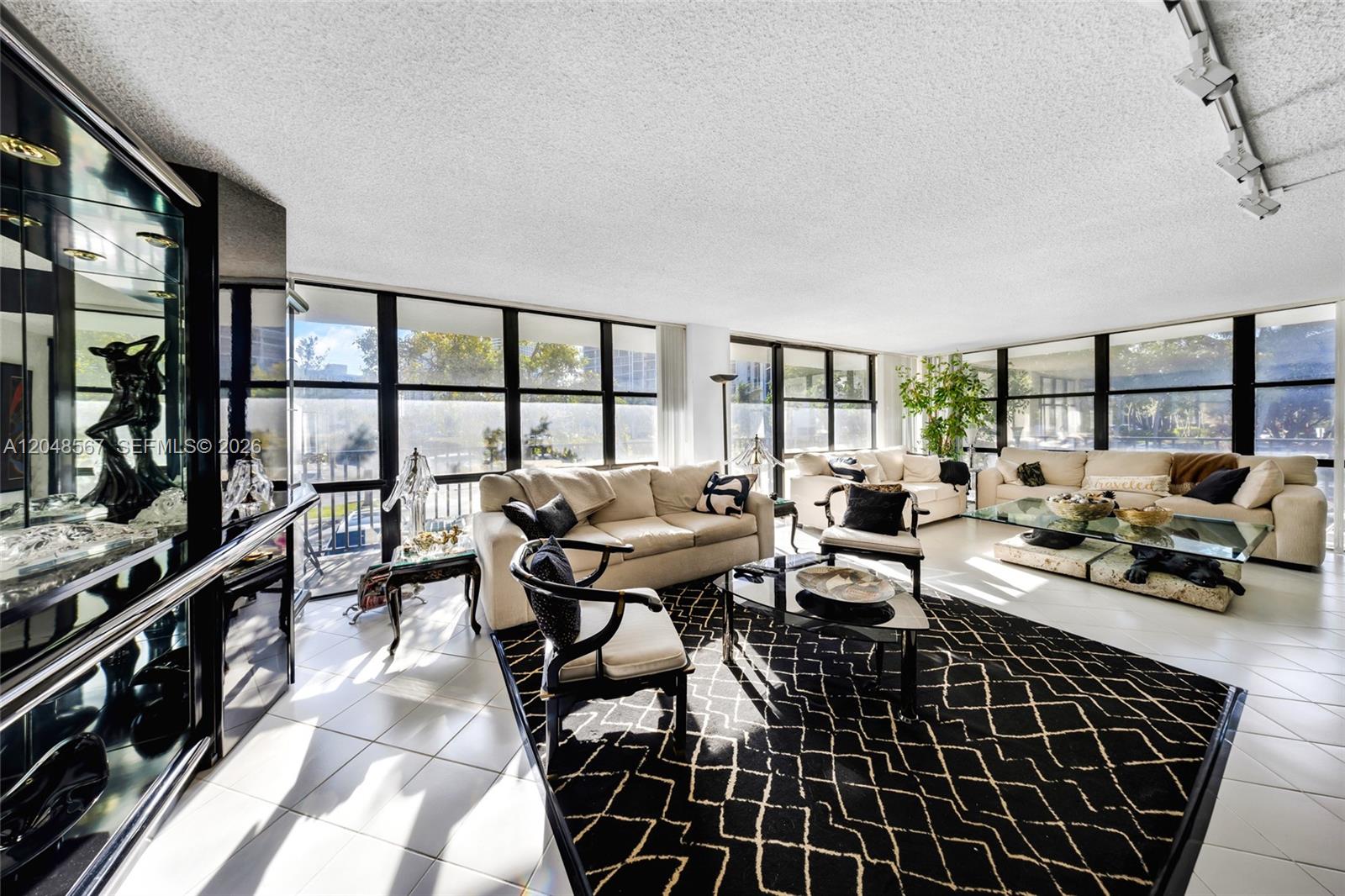 A bright living room features white tile floors, a geometric rug, and floor-to-ceiling windows — 800 Parkview Dr # 230, Hallandale Beach FL 33009, HALLANDALE BEACH, FL