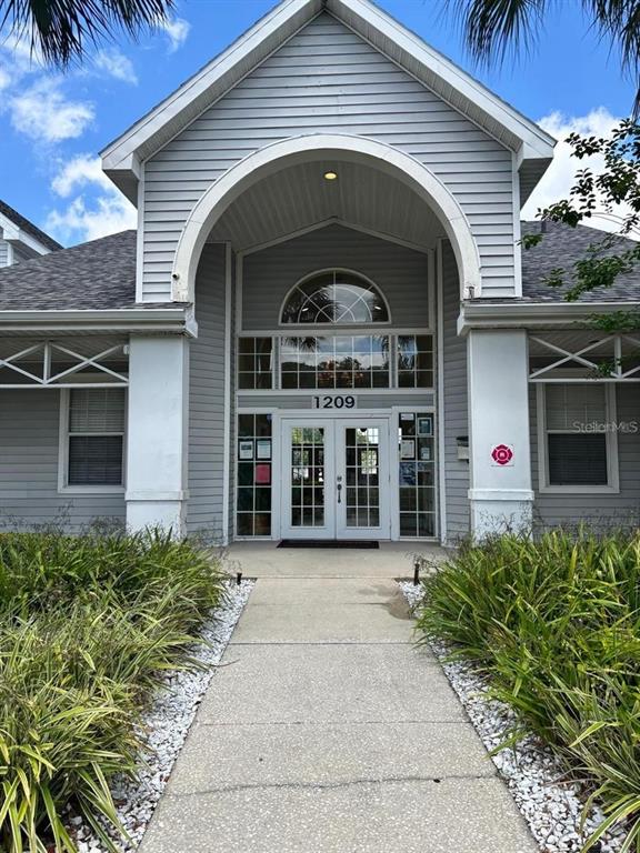 A gray-sided building features a prominent arched entryway with double glass doors and white trim — 1226 BERMUDA LAKES LANE UNIT 303, KISSIMMEE, FL