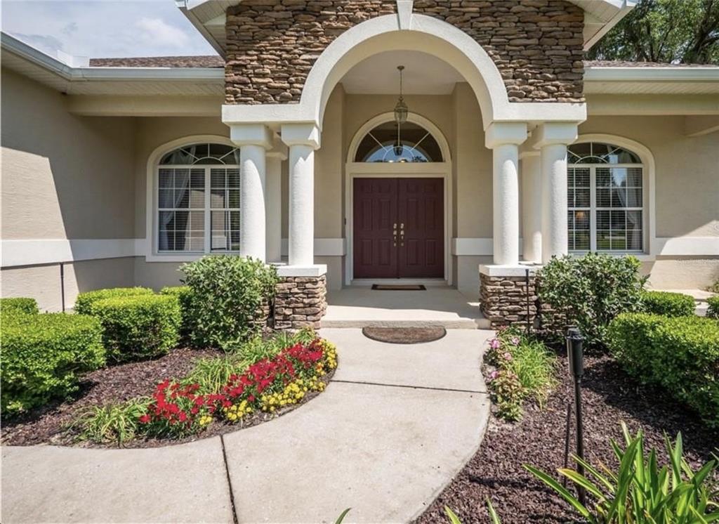 The front entrance of a house features a stone archway, white columns, and double doors — 4541 NW 76TH COURT, OCALA, FL