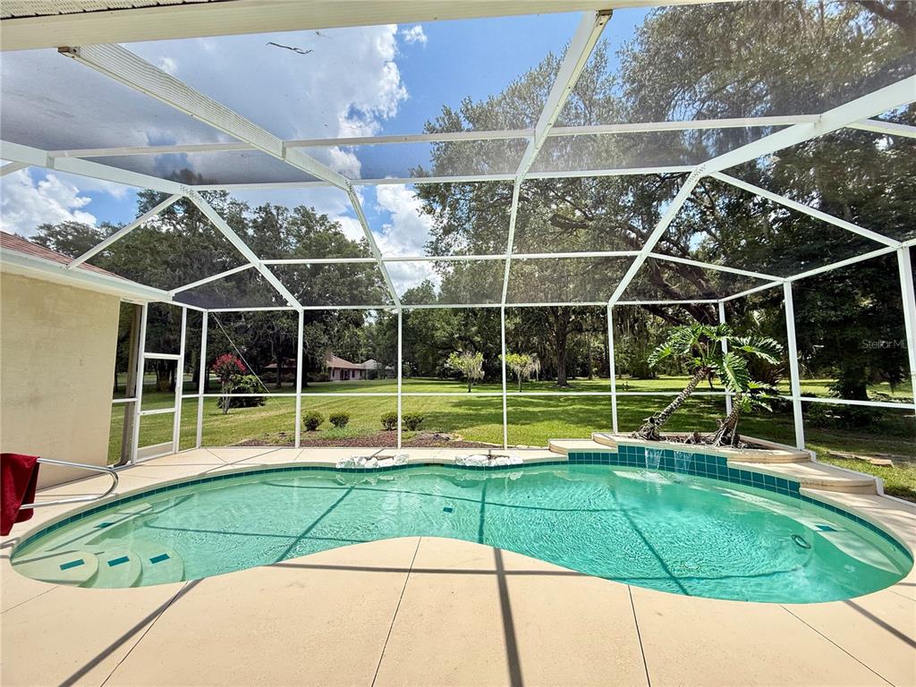 A screened-in swimming pool with a waterfall feature overlooks a large, grassy backyard — 4541 NW 76TH COURT, OCALA, FL
