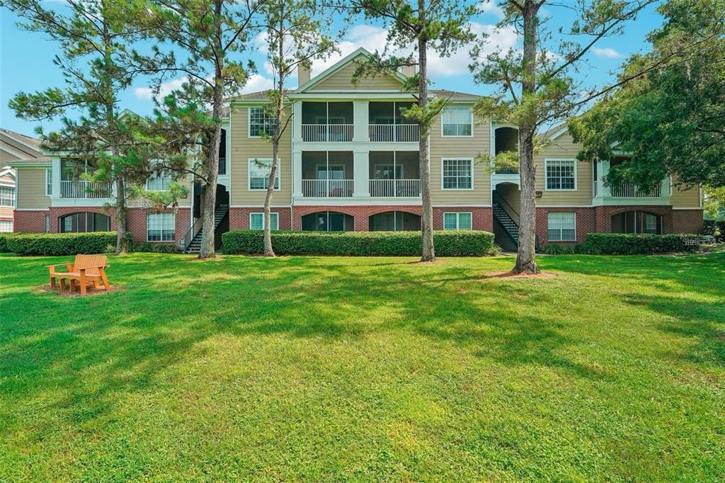 A three-story apartment building with tan siding, brick accents, and screened balconies overlooks a lawn — 13001 MULBERRY PARK DR UNIT 112, ORLANDO, FL