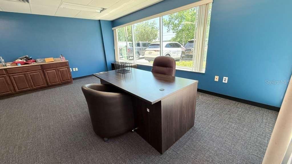 An office features a dark wood desk, two chairs, and blue walls with large windows — 4333 SILVER STAR ROAD UNIT 17, ORLANDO, FL