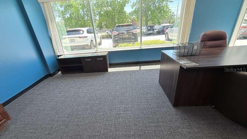 An office with blue walls, gray carpet, a dark desk, and large windows overlooking cars — 4333 SILVER STAR ROAD UNIT 17, ORLANDO, FL