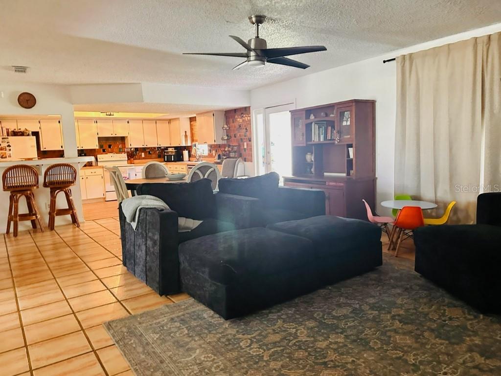 An open-concept living room with tile floors, a dark sectional sofa, and an adjacent kitchen — 1831 KIM ACRES LANE, DOVER, FL
