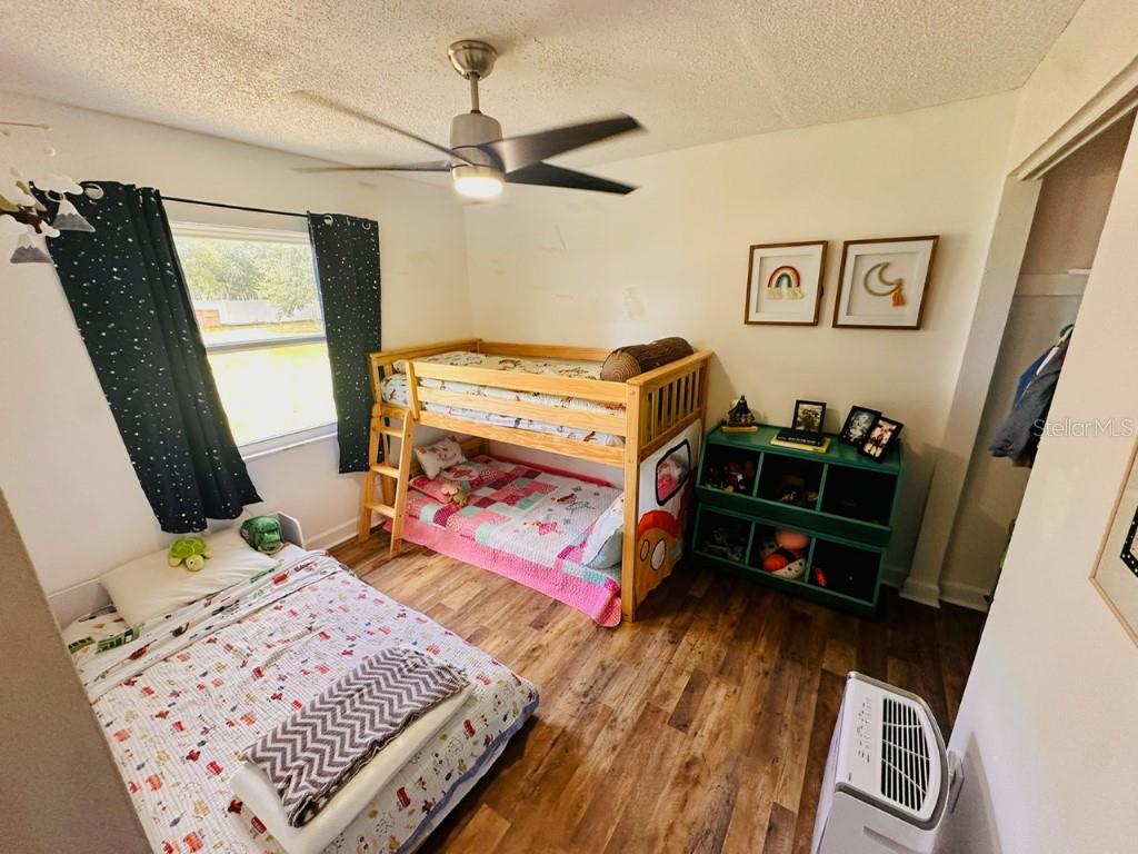 A bedroom features a bunk bed, a twin bed, a green storage unit, and wood flooring — 1831 KIM ACRES LANE, DOVER, FL