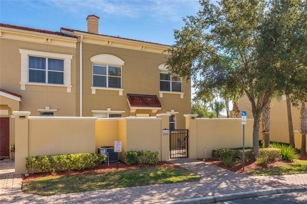 A two-story tan townhouse features a gated courtyard entrance and a brick paver walkway — 2616 BELLA VISTA DRIVE, DAVENPORT, FL
