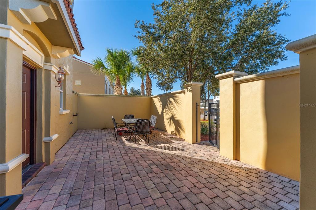 A paved patio area features a dining set enclosed by tan stucco walls and trees — 2616 BELLA VISTA DRIVE, DAVENPORT, FL