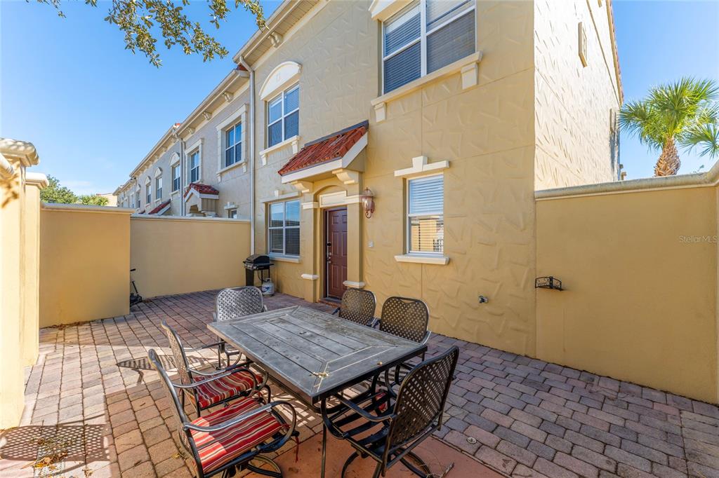 A paved patio with a dining set sits outside a tan two-story townhouse — 2616 BELLA VISTA DRIVE, DAVENPORT, FL