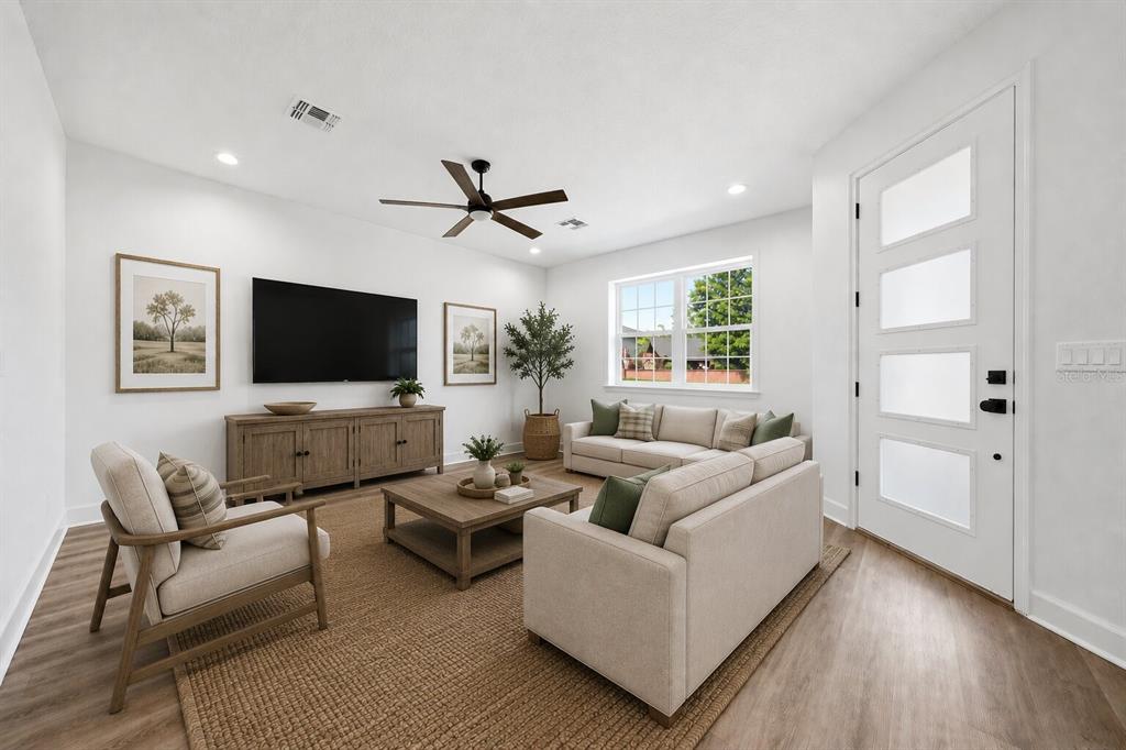A living room features light-colored sofas, a wooden coffee table, a television, and a door — 1018 FARMSTEAD STREET, EUSTIS, FL