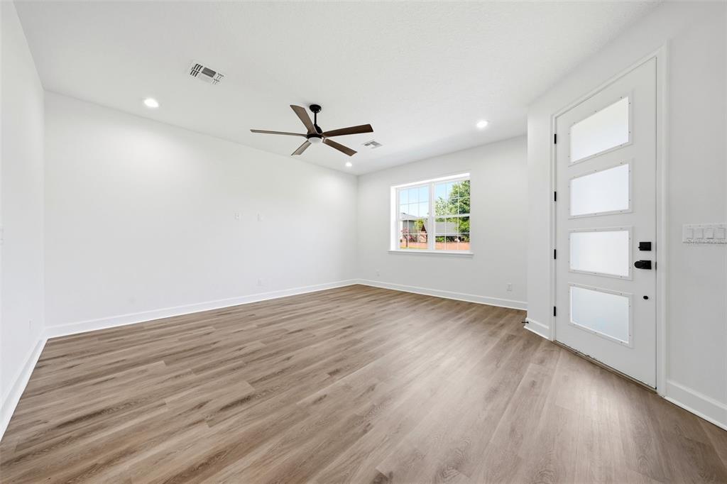 An empty room with white walls, light wood-look flooring, a ceiling fan, and a glass-paneled door — 1018 FARMSTEAD STREET, EUSTIS, FL